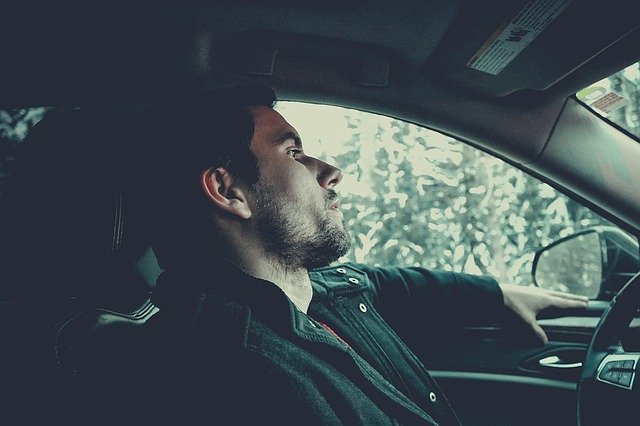 Photo of a young white bearded man sat behind the steering wheel of a car